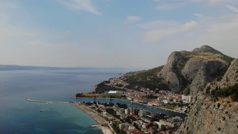 Imágenes-Aéreas-De-Un-Día-Soleado-Y-Brumoso-De-Verano-Sobre-La-Ciudad-De-Omis,-El-Río-Cetina