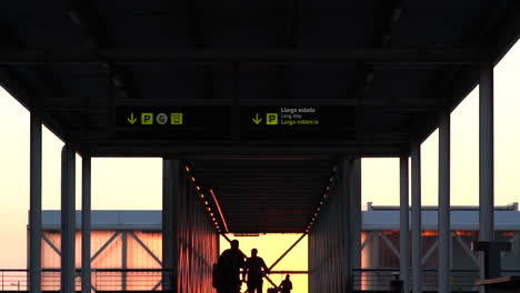 Silueta-De-Personas-Caminando-A-Cámara-Lenta-Por-La-Salida-Del-Aeropuerto-De-Barcelona-Al-Atardecer