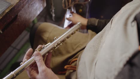 Skilled-instrument-maker-repairing-flute-keys-on-transverse-flute-with-screwdriver,-then-checking-whether-they-close-properly-with-special-tube-light