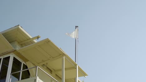 Weiße-Fahne-über-Der-Rettungsschwimmerstation-Am-Strand-Weht-Im-Sommer-Im-Wind