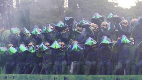 Day-of-the-Dead-Parade---Performers-sitting-on-a-float-are-all-wearing-a-skeleton-mask-and-a-blue,green-iridescent-costume