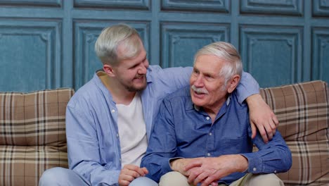 Family-of-senior-father-and-adult-son-or-grandson-having-conversation-chatting-relaxing-on-couch