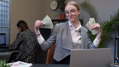 Businesswoman-company-manager-celebrating-success,-dancing-with-stack-of-money-dollar-cash-in-office