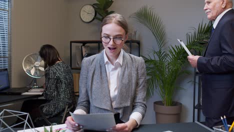 Young-shocked-business-woman-accountant-reading-documents-analyzing-financial-papers-raising-hands