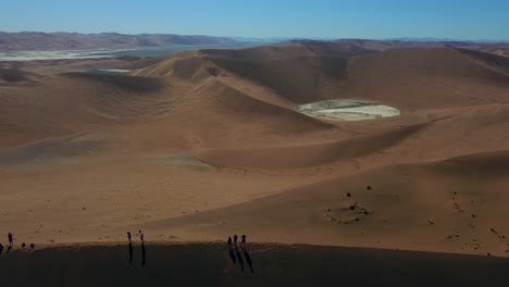 Drohnenaufnahme-Der-Namibwüste-In-Namibia---Drohne-Fliegt-über-Eine-Hohe-Düne-Mit-Reisenden-Und-Wanderern-Auf-Der-Spitze