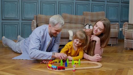 Joven-Madre-Y-Padre-Jugando-Con-Su-Hija-Montando-Un-Tren-De-Juguete-En-Un-Juego-De-Ferrocarril-De-Madera-En-Casa