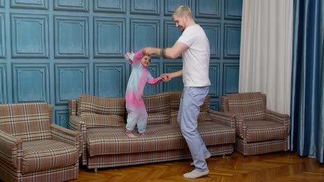 Happy-funny-family-father-and-child-kid-daughter-dancing,-jumping-on-sofa,-listening-music-at-home