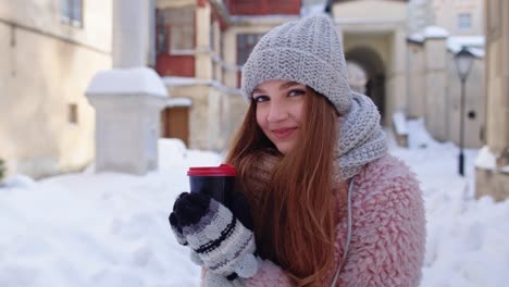 Stylish-woman-traveler-with-hot-drink-in-cup-looking-around-through-city-street-during-vacations