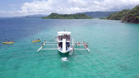 Aerial-view-of-Tourists-having-fun-sliding-off-a-double-decker-boat-slide-and-Kayaking-on-turquoise-water-at-Philippines,-Palawan