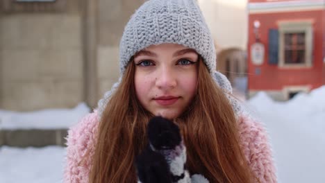 Smiling-traveler-girl-rubs-her-hands-in-gloves-trying-to-keep-warm-in-frosty-weather-on-city-street