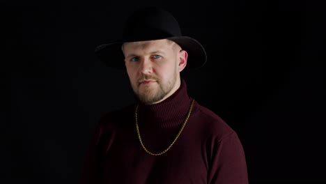 Portrait-of-seductive-smiling-young-man-in-trendy-stylish-clothes-and-hat-against-black-background