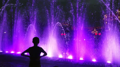 Xian,-China---Julio-De-2019:-Un-Niño-No-Identificado-Admira-El-Increíble-Espectáculo-De-Luz-Y-Sonido-En-Las-Fuentes-De-La-Plaza-Central-De-La-Ciudad-Al-Anochecer