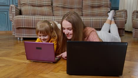 Woman-nanny-and-child-girl-studying-together-with-computer-laptop,-while-lying-on-warm-floor-at-home