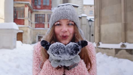 Mujer-Turista-Con-Sombrero-Y-Guantes-Sopla-Nieve-De-Las-Palmas-De-Las-Manos,-Vacaciones-De-Navidad-En-Invierno-Viajando