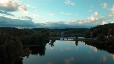 Reflexión-Del-Paisaje-Nuboso-Sobre-Un-Lago-Sereno-Con-Un-Puente-Largo-Rodeado-De-Un-Denso-Y-Exuberante-Bosque-De-Montaña-En-Tleń,-Distrito-De-Gmina-Cekcyn,-Polonia