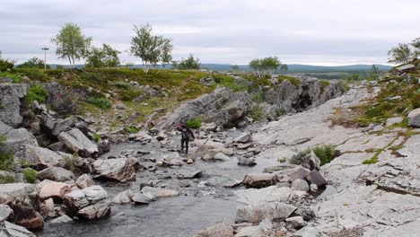 Una-Mujer-Ciclista-De-Montaña-Lleva-Su-Bicicleta-Sobre-Un-Río-En-El-Norte-De-Noruega