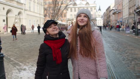 Two-smiling-women-sisters-tourists-walking-together-on-city-street,-young-couple-talking,-embracing