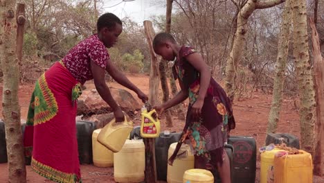 Ein-Junges-Mädchen-Hilft-Ihrer-Mutter,-In-Einem-Halbtrockenen-Gebiet-Mit-Plastikbehältern-Wasser-Zu-Holen