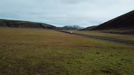 Paisaje-De-Las-Tierras-Altas-De-Islandia,-Vehículo-Todoterreno-En-Movimiento-Por-Una-Carretera-Sucia-En-Un-Valle-Bajo-Colinas-Volcánicas,-Vista-Aérea-De-Seguimiento