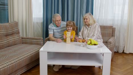 Senior-couple-grandparents-with-child-kid-granddaughter-playing-game-with-wooden-blocks-at-home