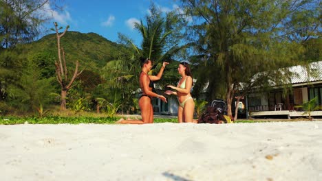 Cute-girls-playing-hands-game-sitting-on-knees-over-white-sand-of-exotic-beach-on-tropical-island-with-green-vegetation-in-Dominican-Republic