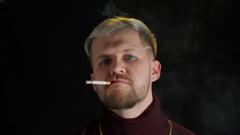 Stylish-addicted-young-man-with-blue-eyes-in-trendy-clothes-looking-at-camera,-smoking-cigarette