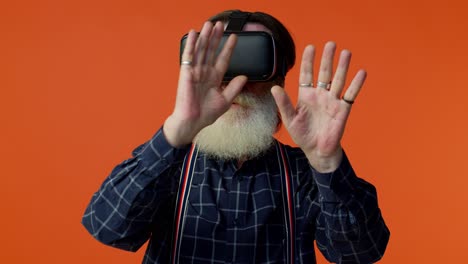 Senior-stylish-gray-haired-man-using-headset-helmet-app-to-play-simulation-virtual-reality-VR-game