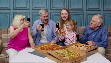 Feliz-Familia-Multigeneracional-Almorzando-En-Casa,-Comiendo-Pizza,-Levantando-Tostadas-Juntos