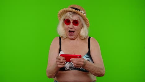 Senior-addicted-woman-tourist-in-red-sunglasses-enjoying-smartphone-gadget-video-games-on-chroma-key