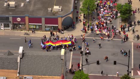 Primer-Plano-Aéreo-De-Una-Gran-Bandera-Del-Orgullo-De-Personas-Celebrando-El-Día-Del-Orgullo-Con-Un-Desfile