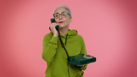 Senior-granny-gray-haired-woman-talking-on-wired-vintage-telephone-of-80s,-says-hey-you-call-me-back