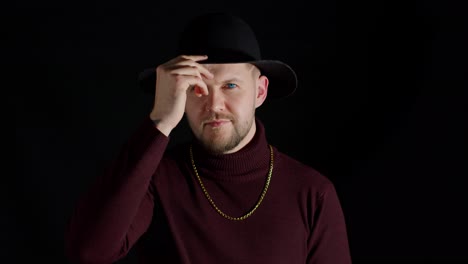 Portrait-of-seductive-smiling-young-man-in-trendy-stylish-clothes-and-hat-against-black-background