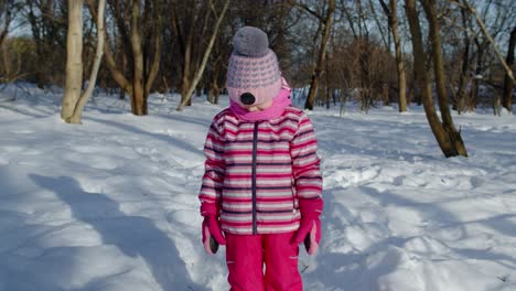 Child-girl-looking-at-camera,-starting-laughing,-fooling-around,-smiling-in-winter-snow-park-forest