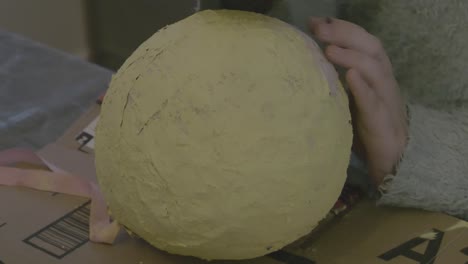 A-close-shot-of-a-girl-sponge-painting-some-yellow-paint-onto-some-paper-mache