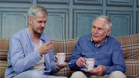 Different-male-generations-family-of-senior-father-and-adult-son-or-grandson-relaxing,-drinking-tea