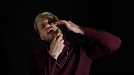 Portrait-of-unshaven-young-man-in-trendy-stylish-clothes-shaving-with-knife-against-black-background