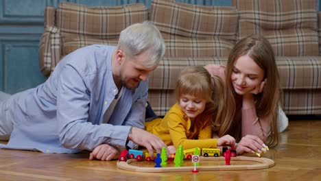 Joven-Madre-Y-Padre-Jugando-Con-Su-Hija-Montando-Un-Tren-De-Juguete-En-Un-Juego-De-Ferrocarril-De-Madera-En-Casa