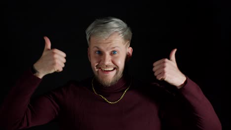 Smiling-man-in-stylish-blouse-looking-approvingly-at-camera-showing-thumbs-up-on-black-background