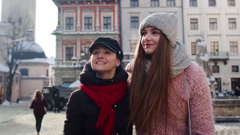 Two-smiling-women-sisters-tourists-walking-together-on-city-street,-couple-talking,-embracing