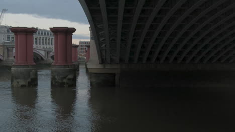 Underneath-London-Blackfriars-Railway-Station-Bridge-Arches,-River-Thames-with-Red-Pillars-from-Old-Bridge,-100-Victoria-Embankment-in-Background