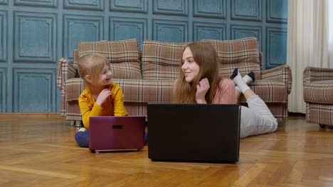 Woman-nanny-and-child-girl-studying-together-with-computer-laptop,-while-lying-on-warm-floor-at-home