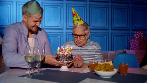 Big-family-celebrating-senior-grandfather-birthday,-making-a-wish-and-blowing-on-candles-at-home