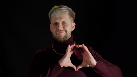 Hombre-Sonriente-Y-Elegante-Con-Ojos-Azules-Mostrando-Forma-De-Corazón-Con-Las-Manos-En-Forma-De-Corazón,-Bondad-Humana