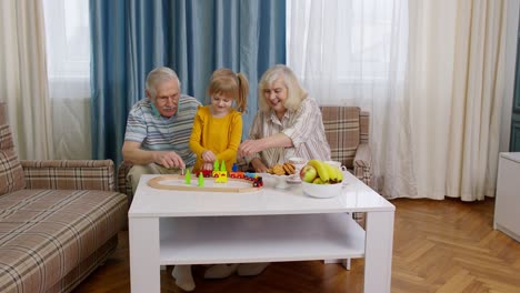 Senior-grandparents-with-child-kid-granddaughter-playing-game,-riding-toy-train-on-railway-at-home