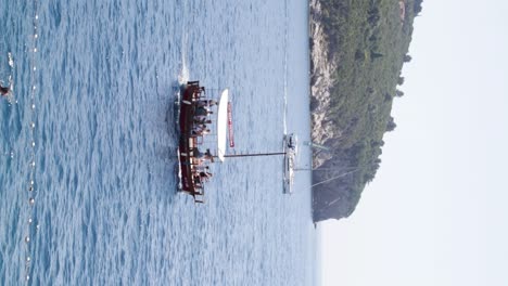 Un-Barco-Taxi-Cargado-De-Turistas-Regresa-Al-Puerto-Del-Casco-Antiguo,-Con-Un-Velero-Croata-Y-La-Isla-De-Lokrum-Al-Fondo