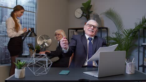 Cheerful-senior-company-boss-or-manager-laughing-and-being-surprised-with-colleagues-team-in-office