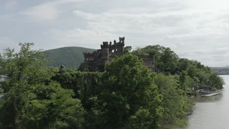 Drone-shot-flying-to-the-right-and-panning-left,-revealing-a-old-castle-behind-the-trees