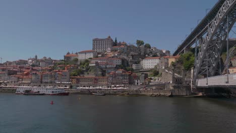 Langsamer-Schwenk-Von-Der-Architektonischen-Stahlbrücke-Luis-Nach-Ribeira-An-Einem-Sonnigen-Europäischen-Tag-Mit-Segelbooten-Im-Fluss-Duoro,-Porto,-Portugal