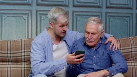 Happy-family-senior-father-and-son-watching-on-mobile-phone-to-internet-online-with-fun-together