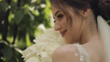 Beautiful-stylish-bride-in-white-wedding-dress-and-veil-holding-wedding-bouquet-in-hands-in-park